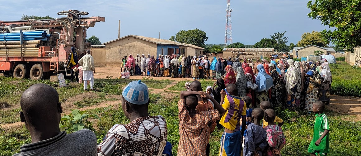 Rural community observing well drilling operation